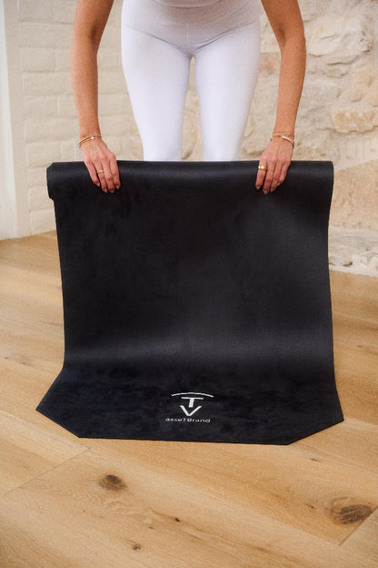 Woman unrolling a black machine-washable yoga mat with non-slip microfiber surface indoors