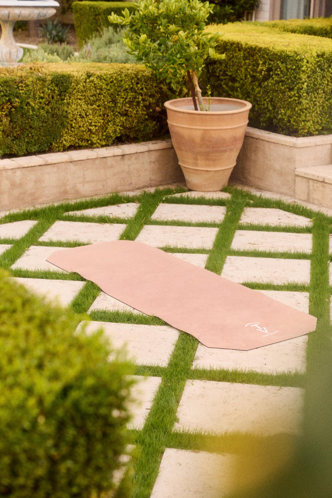 Camel-colored machine-washable yoga mat placed outdoors on stone and grass pathway